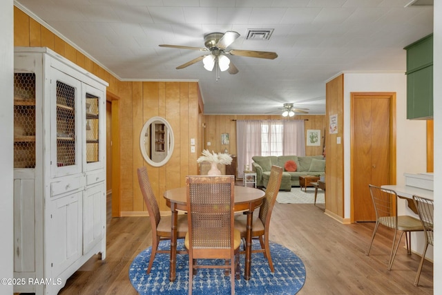 dining space with ceiling fan, wooden walls, wood finished floors, visible vents, and crown molding