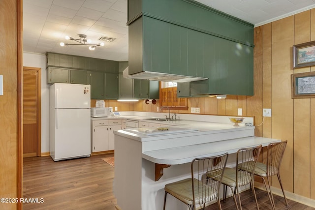 kitchen with white appliances, wood finished floors, a peninsula, light countertops, and a sink