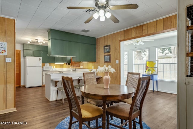 dining area featuring dark wood-style flooring, crown molding, visible vents, a ceiling fan, and wooden walls