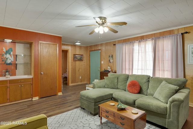 living room featuring light wood-style floors, ceiling fan, crown molding, and wood walls