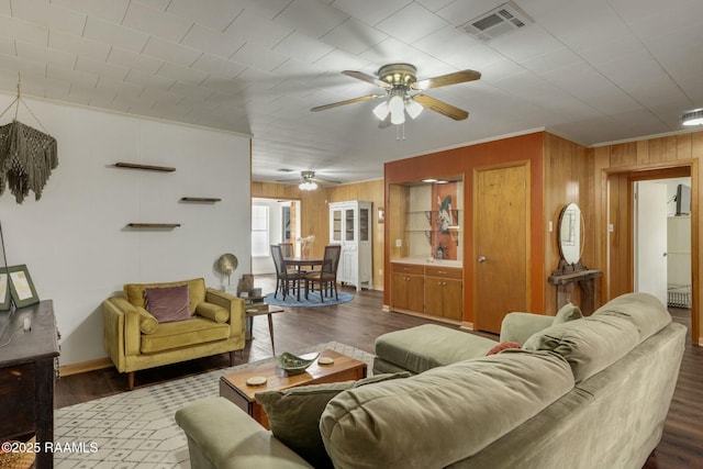 living room with visible vents, crown molding, wooden walls, and wood finished floors