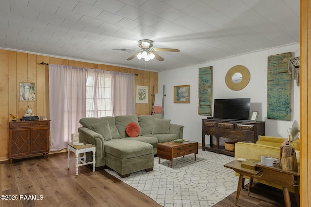 living room featuring wood walls, ceiling fan, crown molding, and wood finished floors