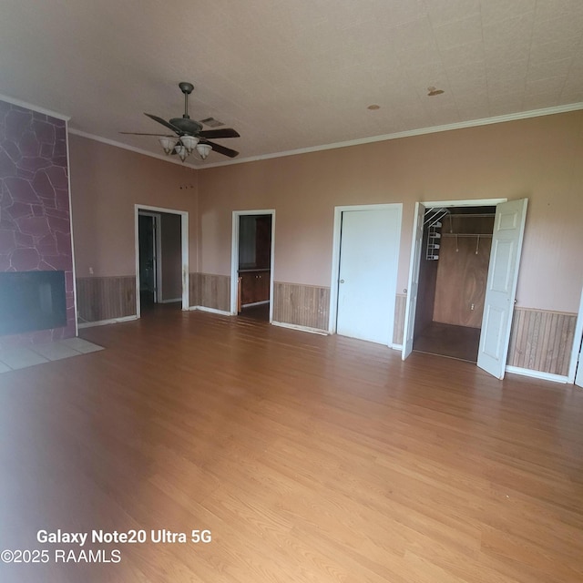 spare room featuring a wainscoted wall, crown molding, a fireplace, and wood finished floors