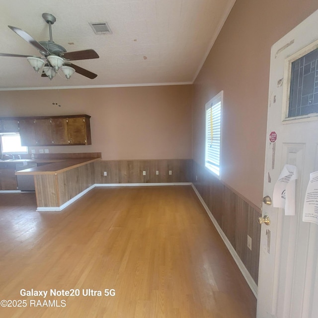 unfurnished living room with a wainscoted wall, crown molding, visible vents, light wood-style floors, and wood walls