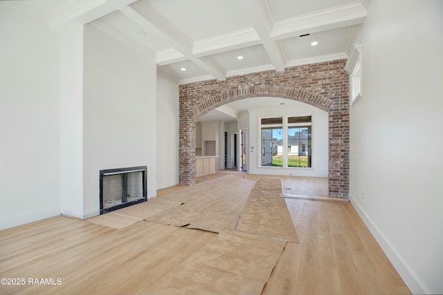 unfurnished living room with crown molding, beamed ceiling, a fireplace, wood finished floors, and arched walkways