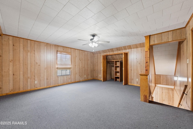 empty room featuring wooden walls, a ceiling fan, baseboards, and carpet floors