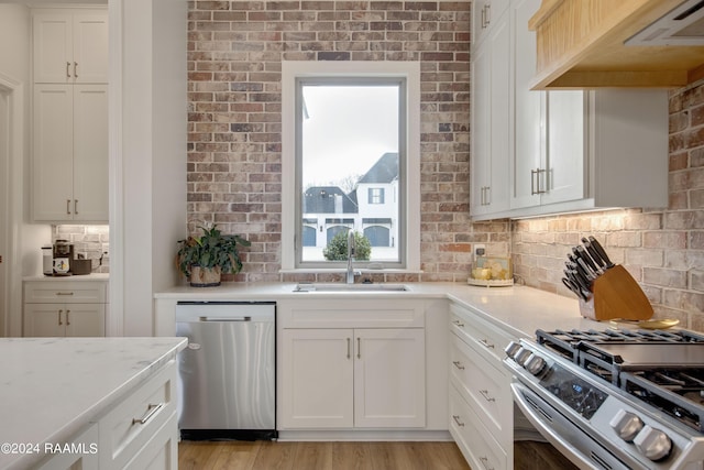 kitchen featuring appliances with stainless steel finishes, range hood, white cabinetry, and a sink