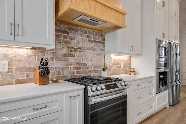 kitchen with stainless steel appliances, light countertops, decorative backsplash, white cabinets, and exhaust hood