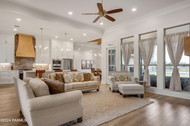 living room with ceiling fan with notable chandelier, ornamental molding, light wood-type flooring, and recessed lighting