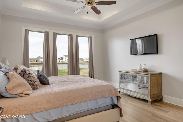 bedroom with multiple windows, a raised ceiling, light wood-style flooring, and crown molding