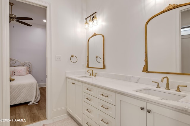 ensuite bathroom featuring double vanity, ceiling fan, a sink, and wood finished floors