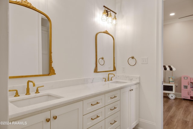 bathroom featuring double vanity, wood finished floors, a sink, and crown molding