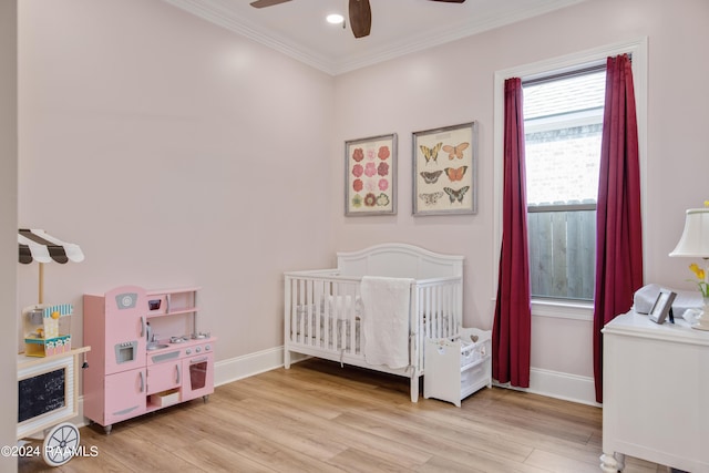 bedroom featuring baseboards, light wood finished floors, a nursery area, and crown molding