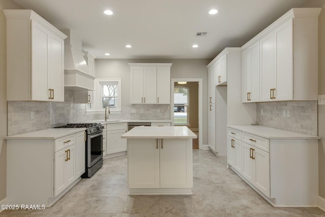 kitchen with custom exhaust hood, light countertops, appliances with stainless steel finishes, white cabinets, and a kitchen island