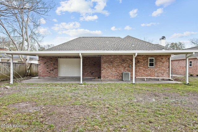 rear view of house with central AC, a shingled roof, brick siding, fence, and a chimney