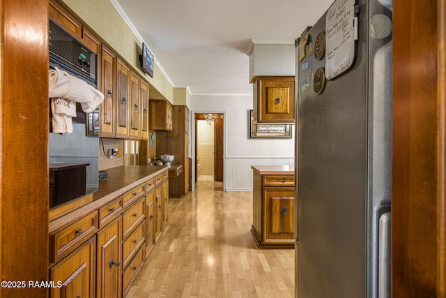 kitchen featuring brown cabinetry, a wainscoted wall, light wood finished floors, and ornamental molding