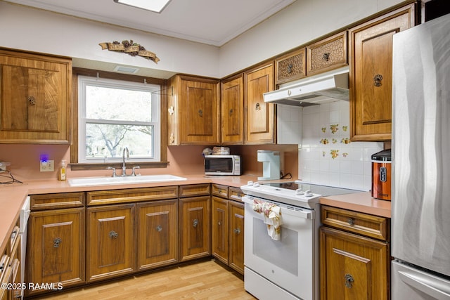 kitchen featuring brown cabinets, under cabinet range hood, a sink, white electric range oven, and freestanding refrigerator