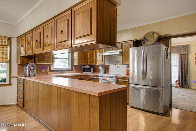 kitchen with a peninsula, stainless steel appliances, under cabinet range hood, crown molding, and brown cabinets