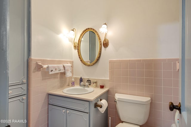 bathroom featuring vanity, tile walls, toilet, and a wainscoted wall