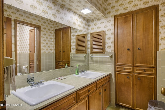 full bathroom with double vanity, wallpapered walls, and a sink