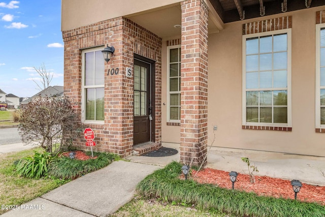 view of exterior entry with stucco siding and brick siding