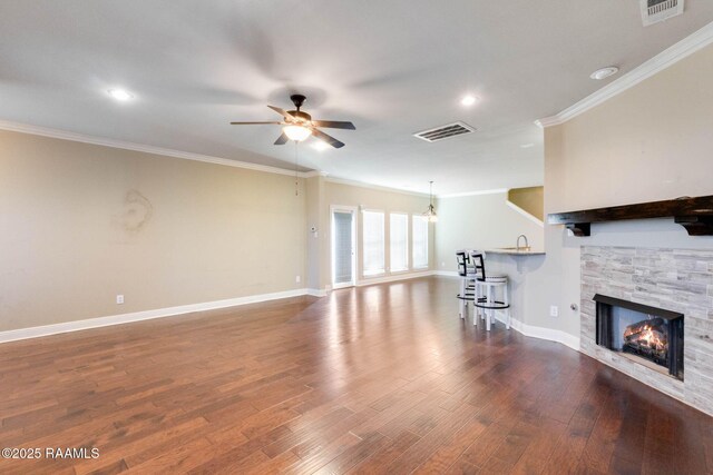 unfurnished living room with a stone fireplace, wood finished floors, visible vents, and ceiling fan