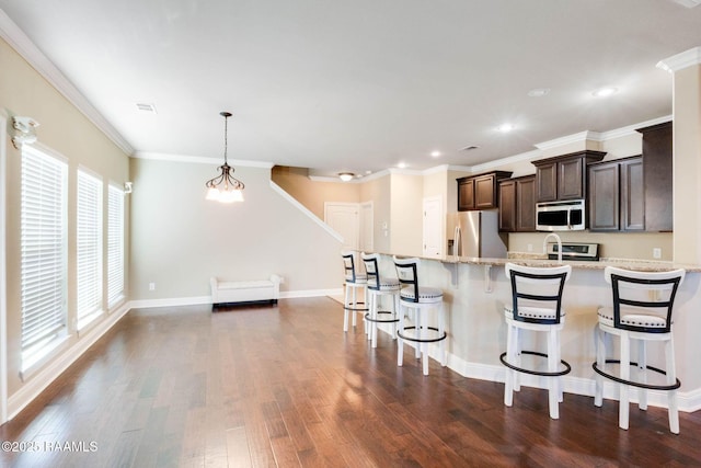 kitchen with dark brown cabinetry, a kitchen bar, ornamental molding, appliances with stainless steel finishes, and dark wood-style flooring