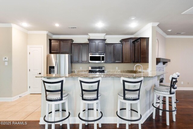 kitchen featuring visible vents, dark brown cabinetry, light stone counters, a peninsula, and stainless steel appliances