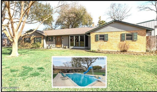 rear view of house with a lawn, an outdoor pool, and brick siding