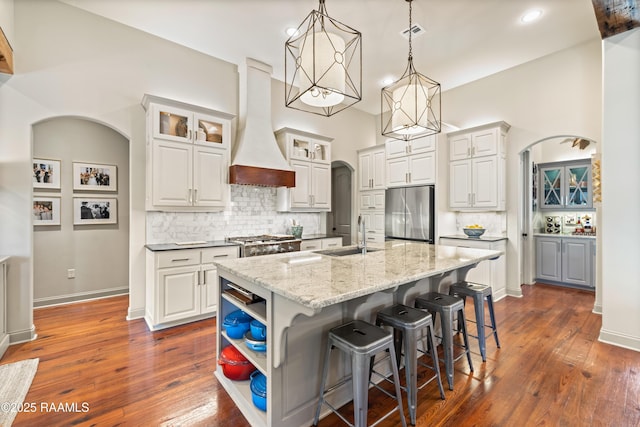 kitchen with stainless steel fridge, arched walkways, range, premium range hood, and a sink