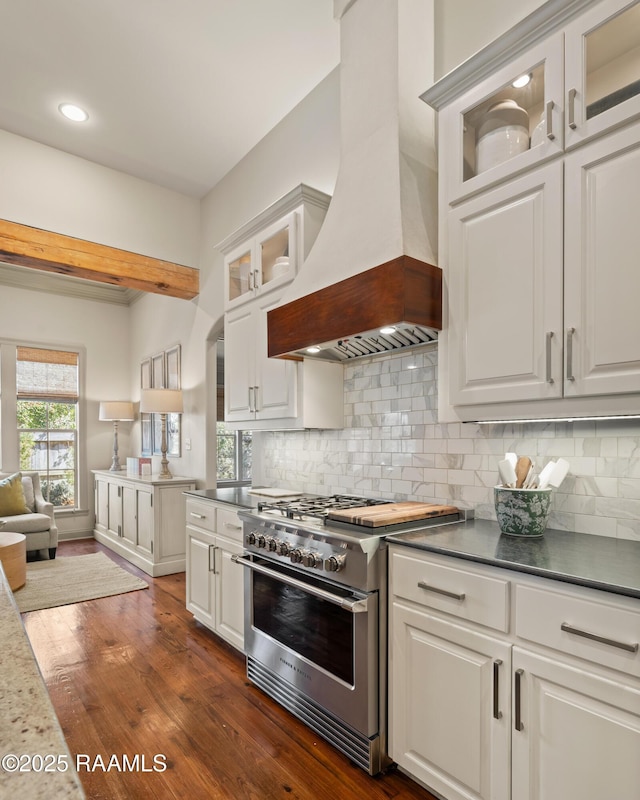 kitchen with premium range hood, white cabinets, high end range, decorative backsplash, and dark wood finished floors