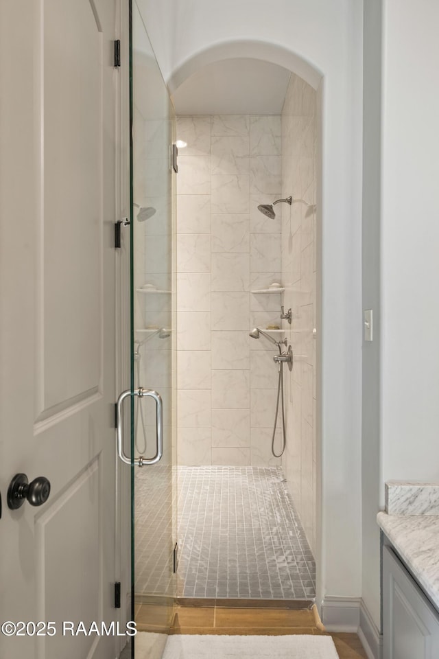 full bathroom with a stall shower, vanity, baseboards, and wood finished floors