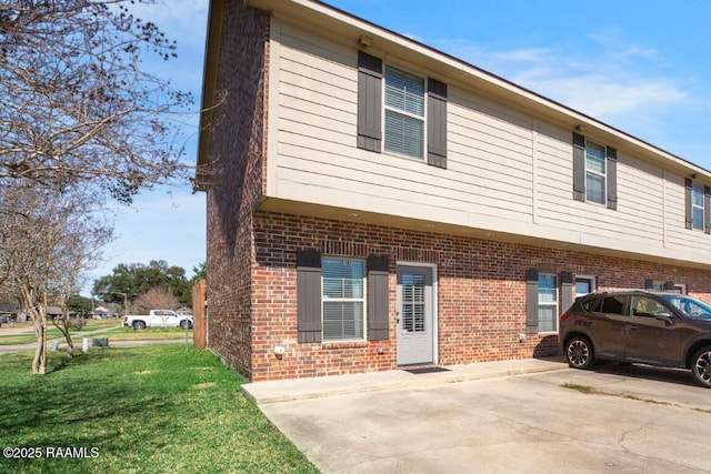 view of property exterior with uncovered parking, a yard, and brick siding