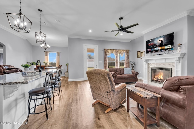 living room with ornamental molding, a glass covered fireplace, light wood-style flooring, and baseboards