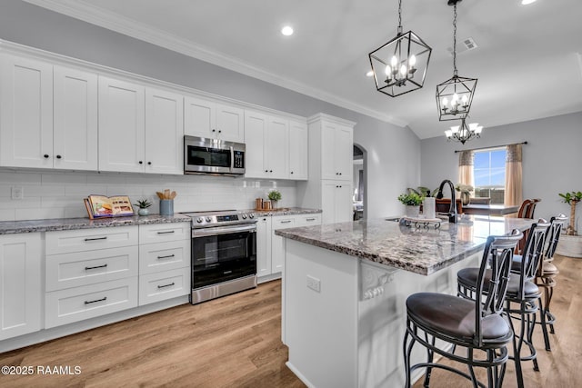 kitchen with arched walkways, light wood-style flooring, stainless steel appliances, visible vents, and crown molding