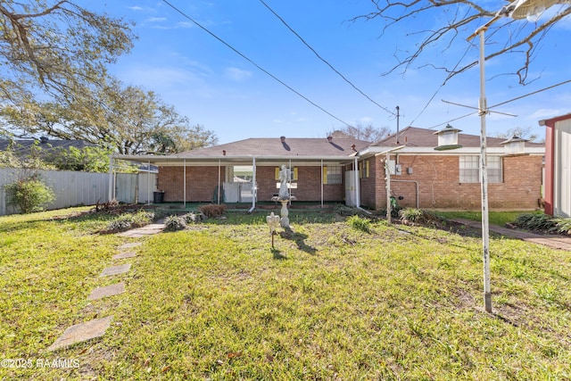 rear view of house featuring brick siding, fence, and a lawn