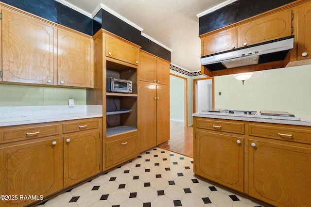 kitchen with brown cabinetry, light floors, light countertops, under cabinet range hood, and white cooktop