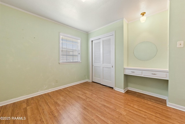 unfurnished bedroom featuring baseboards, built in desk, and light wood-type flooring