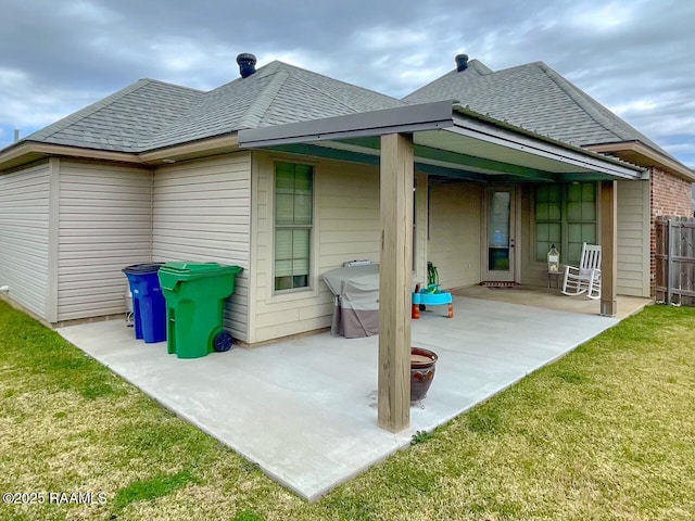 back of house with roof with shingles, a patio area, fence, and a lawn