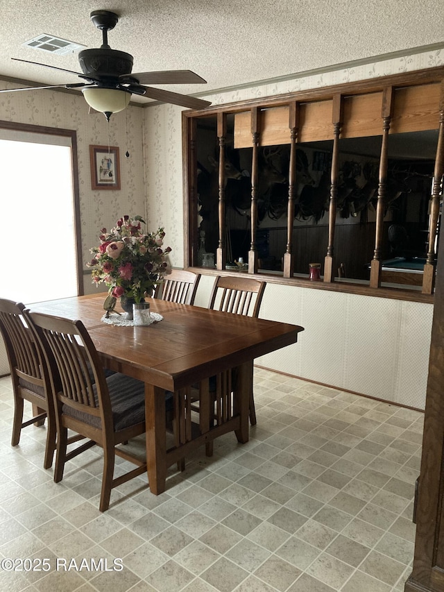 dining room with a textured ceiling, a ceiling fan, visible vents, and wallpapered walls