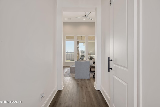 hall featuring dark wood-type flooring, a barn door, and baseboards