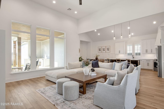 living area with high vaulted ceiling, light wood finished floors, visible vents, and recessed lighting