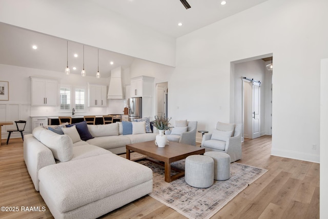 living area featuring light wood-style floors, recessed lighting, a towering ceiling, and a barn door