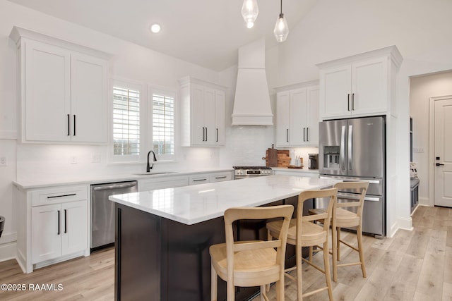 kitchen with premium range hood, white cabinetry, stainless steel appliances, and a sink