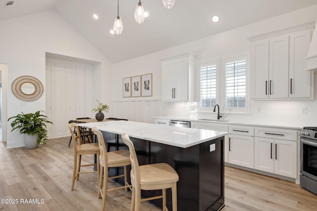 kitchen with white cabinets, a kitchen island, stainless steel appliances, a kitchen bar, and a sink