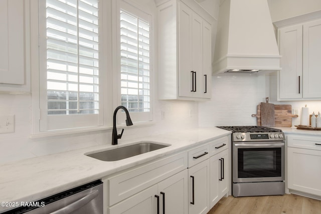 kitchen featuring stainless steel appliances, a sink, light wood-style floors, white cabinets, and custom range hood