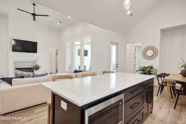 kitchen with high vaulted ceiling, stainless steel microwave, light wood-type flooring, and a tile fireplace