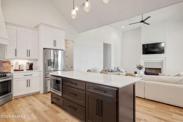 kitchen with open floor plan, appliances with stainless steel finishes, a tile fireplace, and white cabinetry