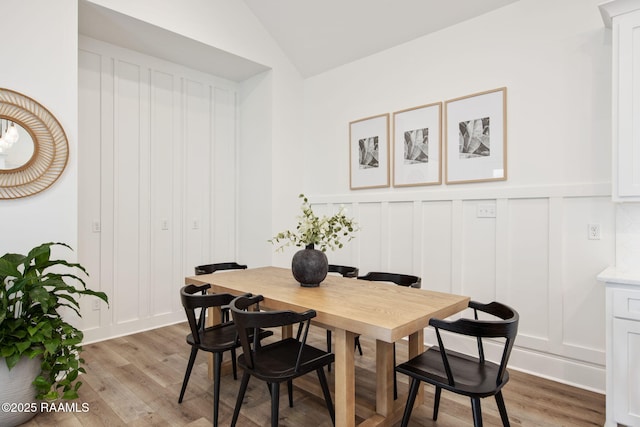 dining space featuring lofted ceiling, a decorative wall, and light wood finished floors