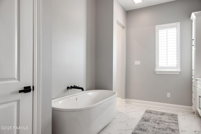 bathroom featuring marble finish floor, baseboards, and a freestanding bath